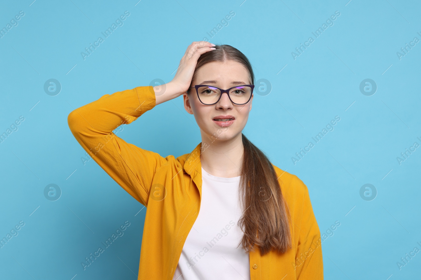 Confused teenage girl on light blue background Photo of Confused teenage girl on light blue background