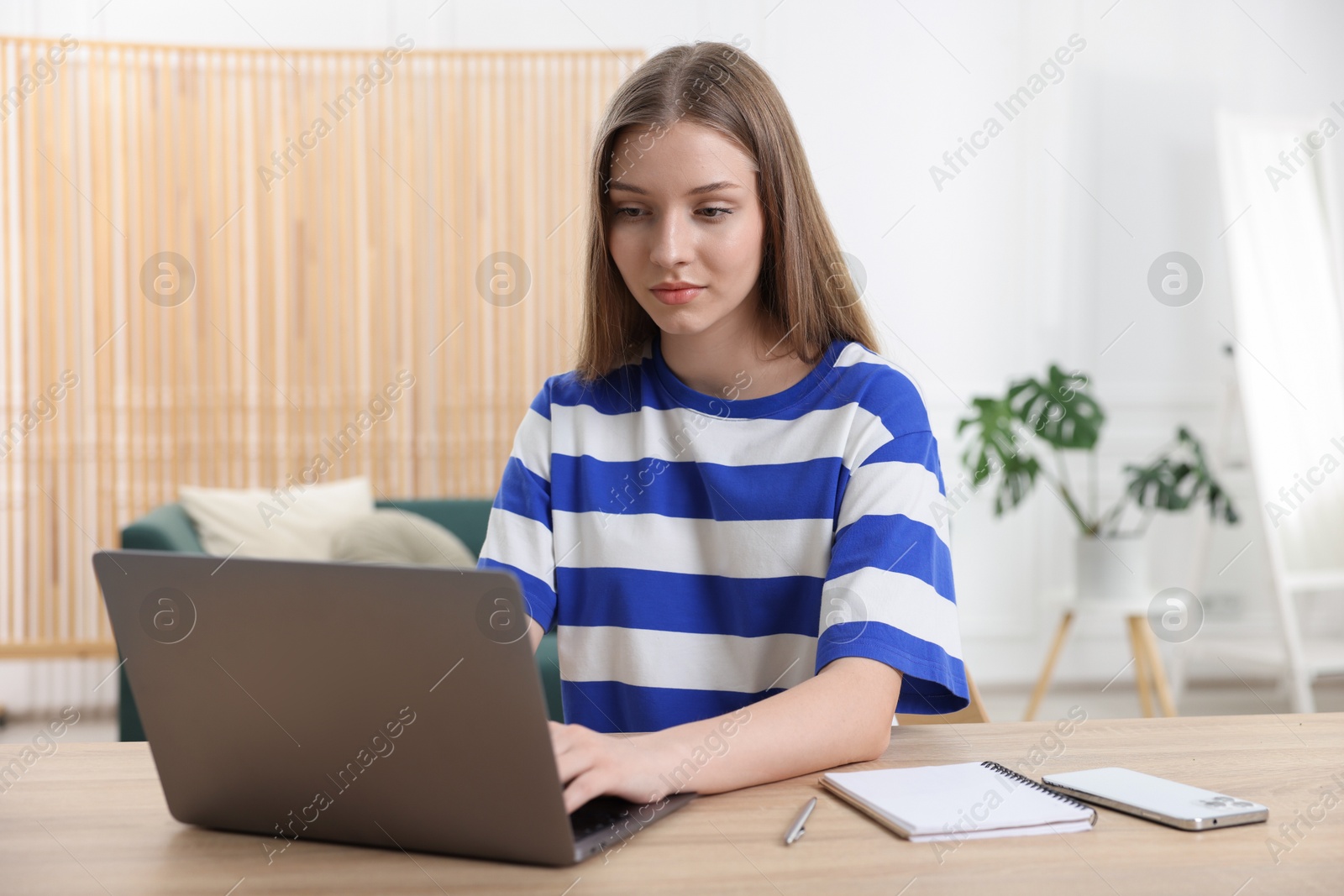 Teenage girl doing homework with laptop at wooden desk indoors Photo of Teenage girl doing homework with laptop at wooden desk indoors