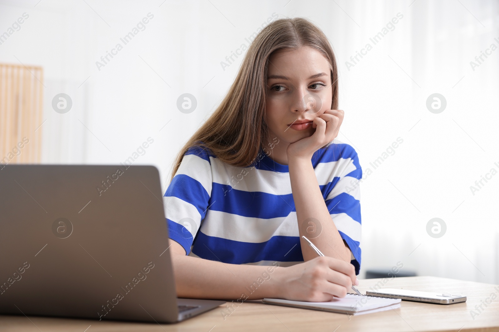 Frustrated teenage girl doing homework with laptop at wooden desk indoors Photo of Frustrated teenage girl doing homework with laptop at wooden desk indoors