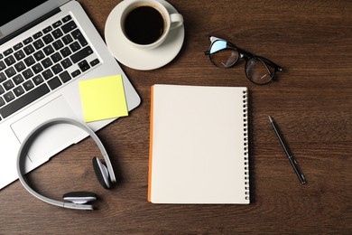 Photo of Notebook, sticky note, pen, headphones, coffee and laptop on wooden table, flat lay