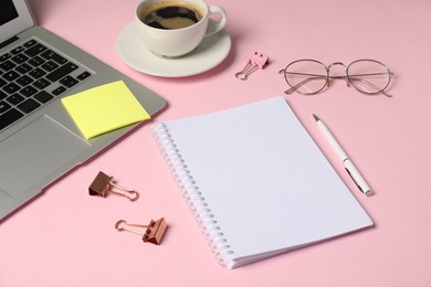 Photo of Notebook, sticky note, pen, binder clips, glasses, coffee and laptop on pink background, closeup