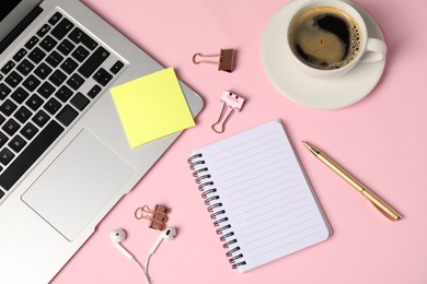 Photo of Notebook, sticky note, pen, binder clips, coffee, earphones and laptop on pink background, flat lay