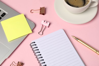 Notebook, sticky note, pen, binder clips, coffee and laptop on pink background, above view