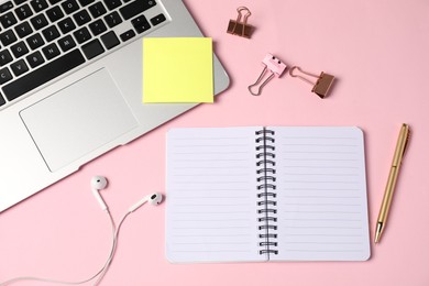 Photo of Notebook, sticky note, pen, binder clips, earphones and laptop on pink background, flat lay