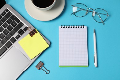 Photo of Notebook, sticky note, pen, binder clip, coffee and laptop on light blue background, flat lay