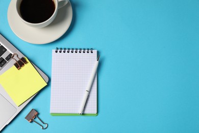 Photo of Notebook, sticky note, pen, binder clips, coffee and laptop on light blue background, flat lay. Space for text