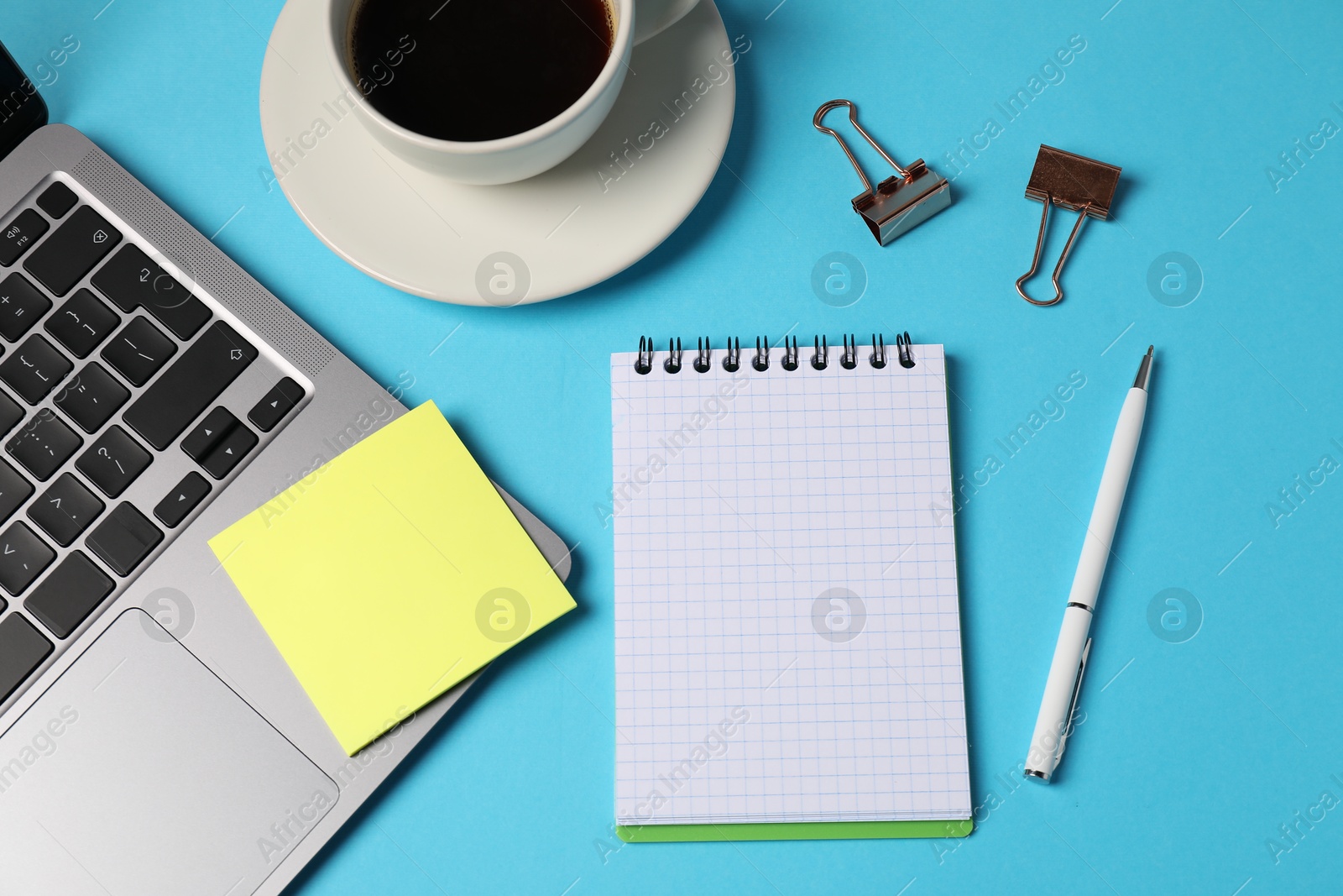 Photo of Notebook, sticky note, pen, binder clips, coffee and laptop on light blue background, flat lay