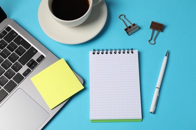 Photo of Notebook, sticky note, pen, binder clips, coffee and laptop on light blue background, flat lay
