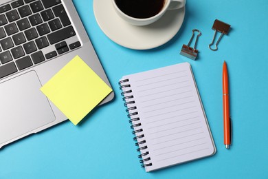 Photo of Notebook, sticky note, pen, binder clips, coffee and laptop on light blue background, flat lay