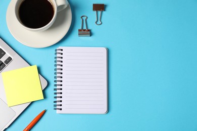 Photo of Notebook, sticky note, pen, binder clips, coffee and laptop on light blue background, flat lay. Space for text