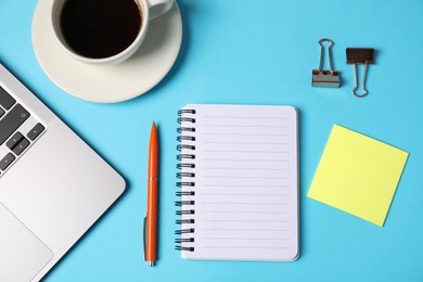 Photo of Notebook, sticky note, pen, binder clips, coffee and laptop on light blue background, flat lay