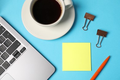 Photo of Sticky note, pen, binder clips, coffee and laptop on light blue background, flat lay