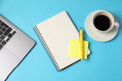 Photo of Notebook, sticky note, pen, coffee and laptop on light blue background, flat lay