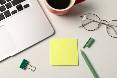 Photo of Sticky note, pen, binder clip, glasses, coffee and laptop on white table, flat lay