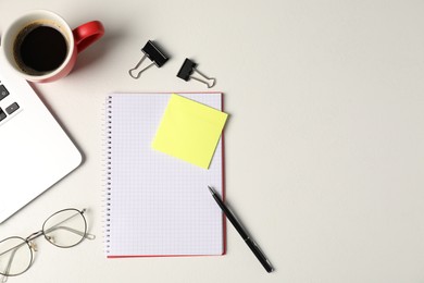 Photo of Notebook, sticky note, pen, binder clips, glasses, coffee and laptop on white table, flat lay. Space for text