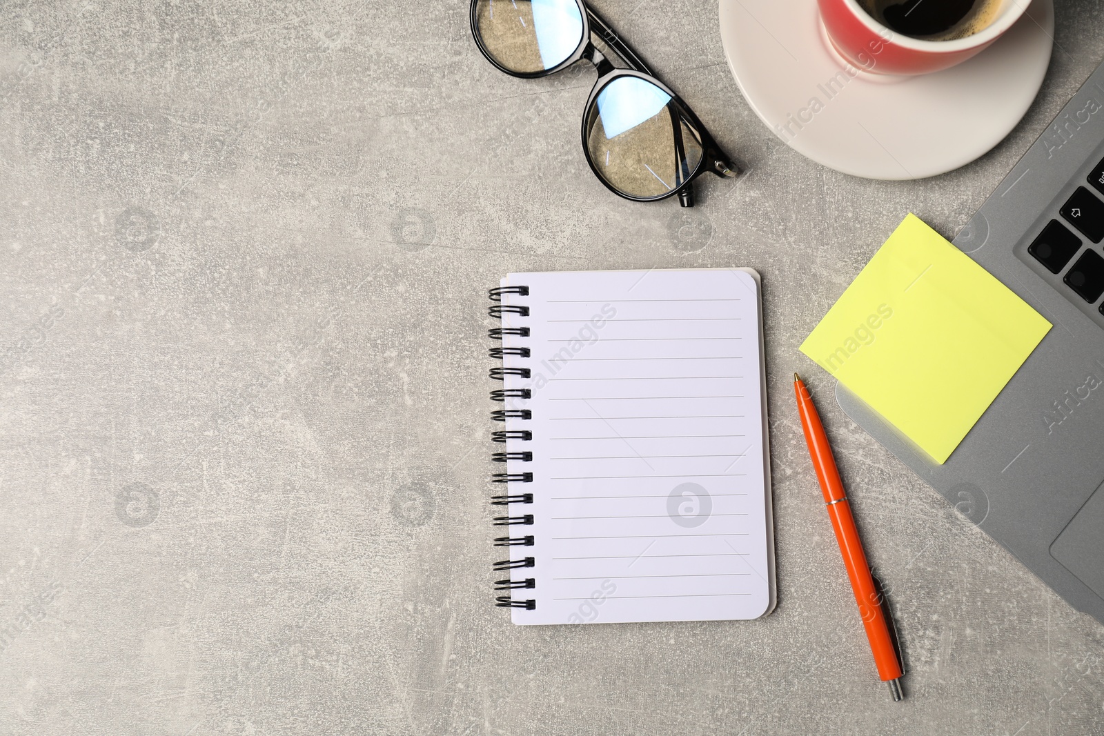 Notebook, pen, sticky note, glasses, coffee and laptop on grey table, flat lay. Space for text Photo of Notebook, pen, sticky note, glasses, coffee and laptop on grey table, flat lay. Space for text