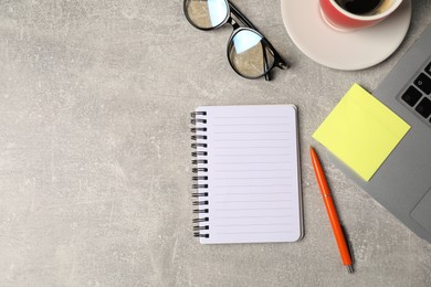 Photo of Notebook, pen, sticky note, glasses, coffee and laptop on grey table, flat lay. Space for text