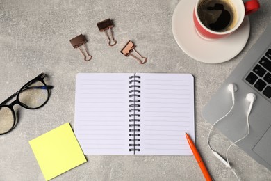 Photo of Notebook, pen, sticky note, glasses, binder clips, earphones, coffee and laptop on grey table, flat lay