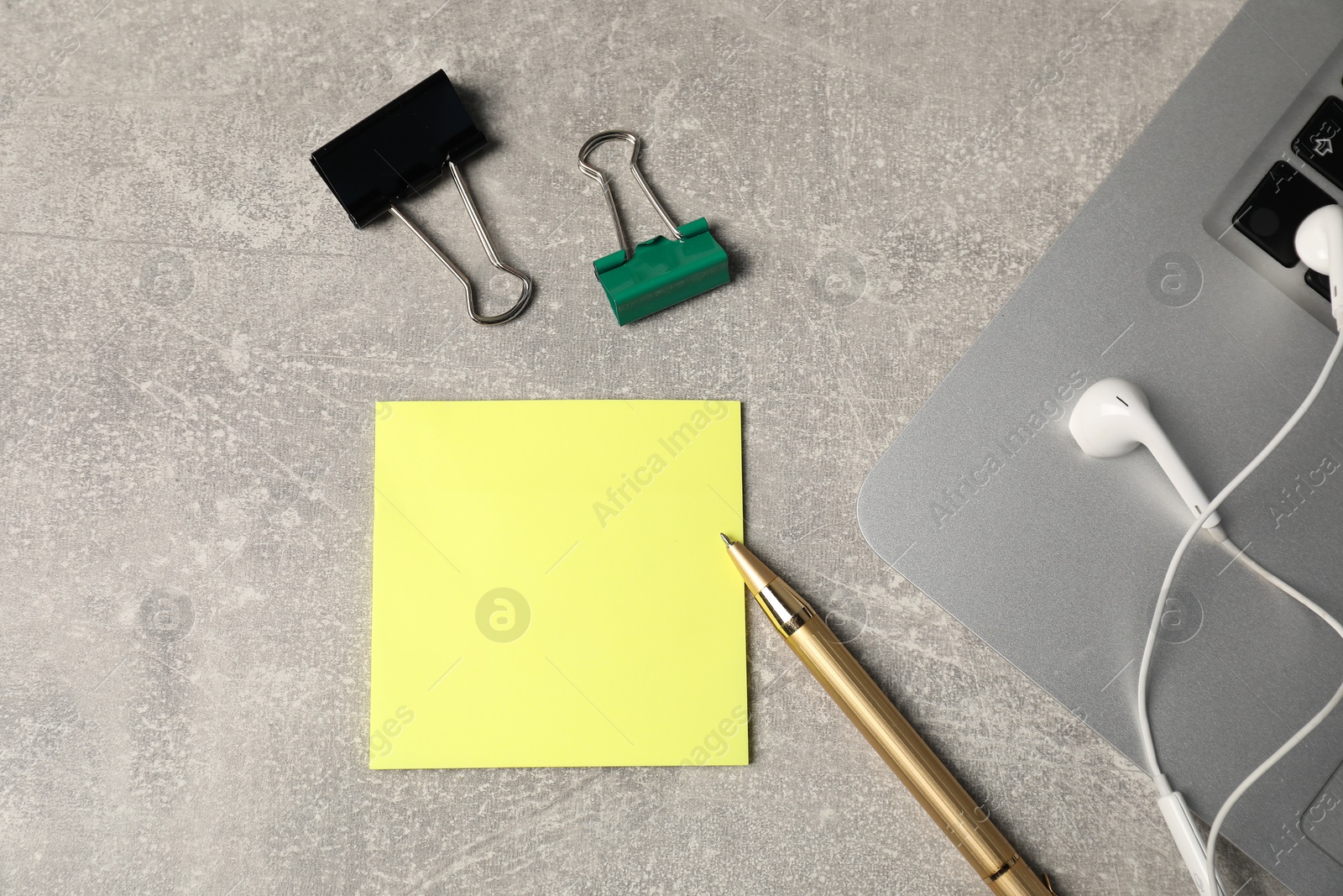 Sticky note, pen, binder clips, earphones and laptop on grey table, flat lay Photo of Sticky note, pen, binder clips, earphones and laptop on grey table, flat lay