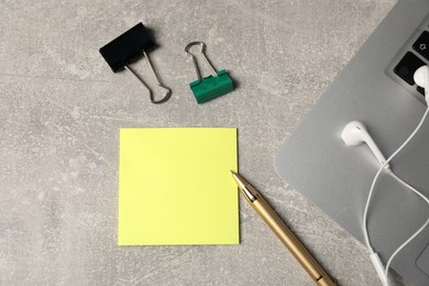 Photo of Sticky note, pen, binder clips, earphones and laptop on grey table, flat lay