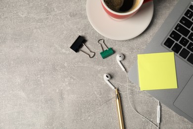 Photo of Sticky note, pen, binder clips, earphones, coffee and laptop on grey table, flat lay. Space for text