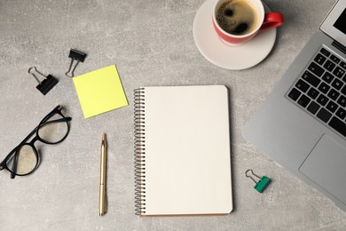 Photo of Notebook, pen, sticky note, binder clips, glasses, coffee and laptop on grey table, flat lay