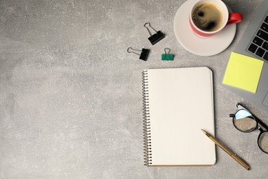 Photo of Notebook, pen, sticky note, binder clips, glasses, coffee and laptop on grey table, flat lay. Space for text