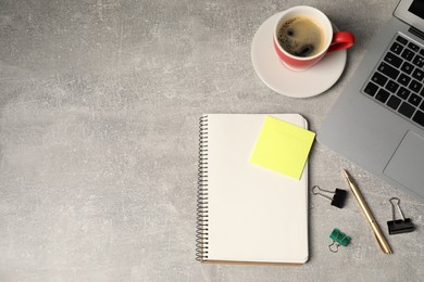 Photo of Notebook, pen, sticky note, binder clips, coffee and laptop on grey table, flat lay. Space for text