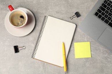 Photo of Notebook, pen, sticky note, binder clips, coffee and laptop on grey table, flat lay