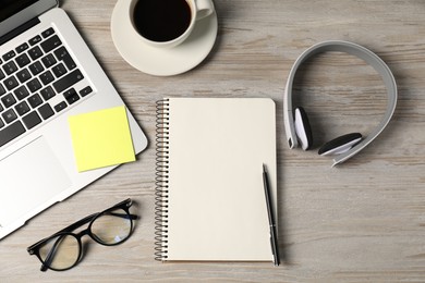 Photo of Notebook, pen, sticky note, headphones, glasses, coffee and laptop on wooden table, flat lay
