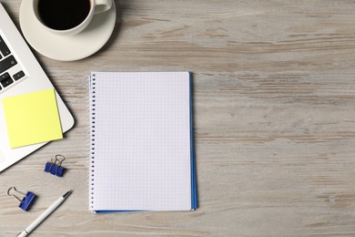 Photo of Notebook, pen, sticky note, binder clips, coffee and laptop on wooden table, flat lay. Space for text