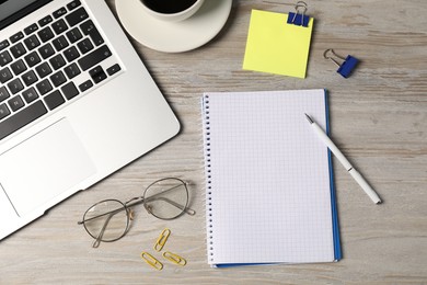 Photo of Notebook, other stationery, glasses, coffee and laptop on wooden table, flat lay
