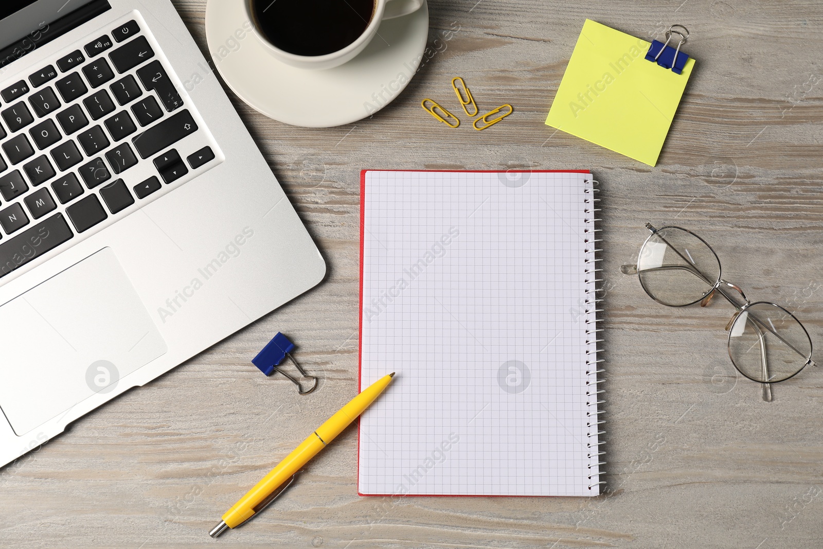 Photo of Notebook, other stationery, glasses, coffee and laptop on wooden table, flat lay