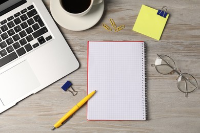 Photo of Notebook, other stationery, glasses, coffee and laptop on wooden table, flat lay
