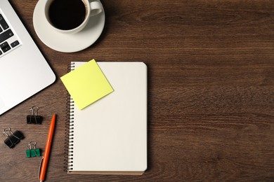 Photo of Notebook, pen, sticky note, binder clips, coffee and laptop on wooden table, flat lay. Space for text