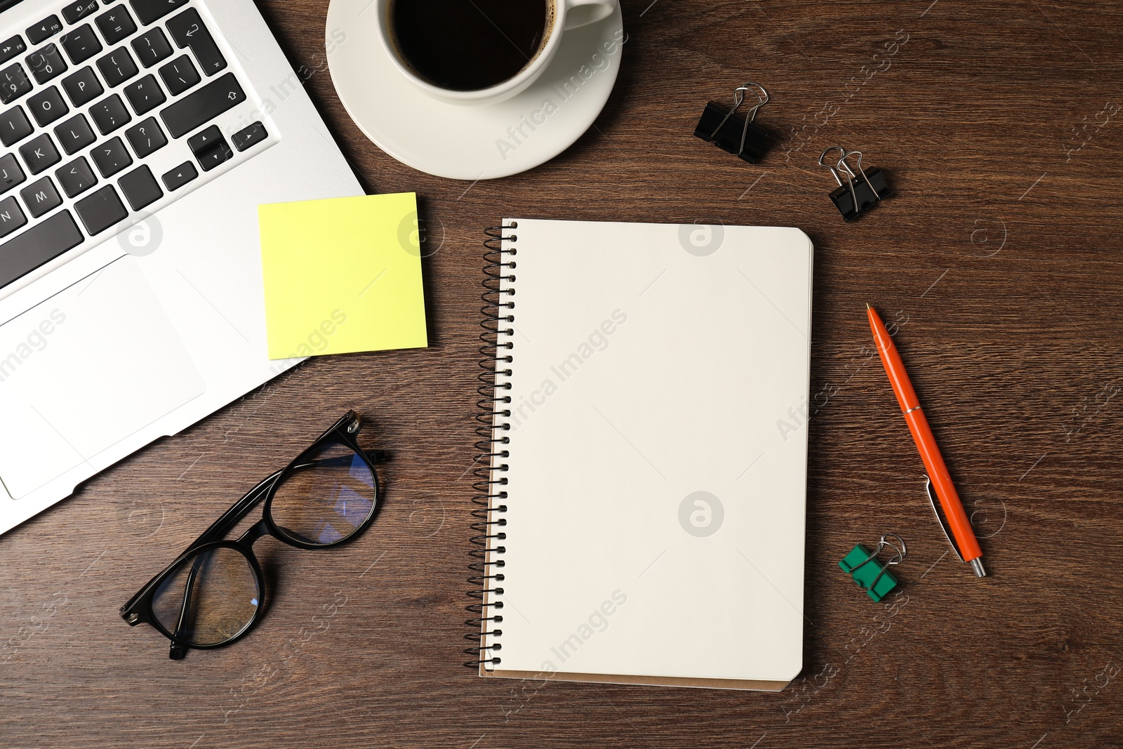 Notebook, pen, sticky note, binder clips, glasses, coffee and laptop on wooden table, flat lay Photo of Notebook, pen, sticky note, binder clips, glasses, coffee and laptop on wooden table, flat lay