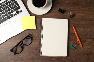 Photo of Notebook, pen, sticky note, binder clips, glasses, coffee and laptop on wooden table, flat lay
