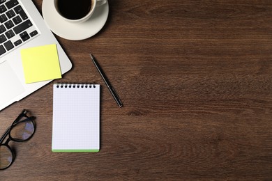 Photo of Notebook, pen, sticky note, glasses, coffee and laptop on wooden table, flat lay. Space for text