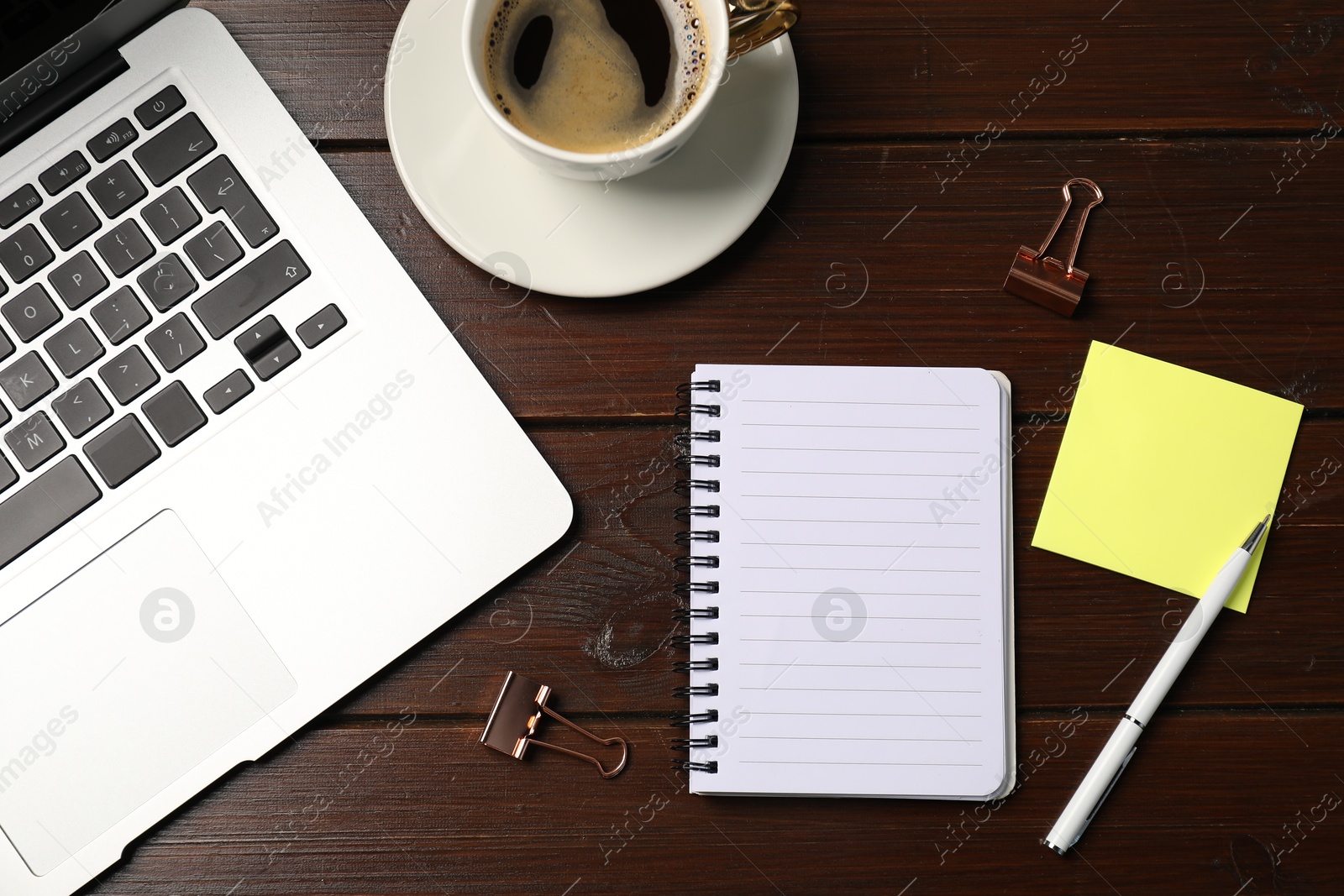 Notebook, sticky note, pen, binder clips, coffee and laptop on wooden table, flat lay Photo of Notebook, sticky note, pen, binder clips, coffee and laptop on wooden table, flat lay