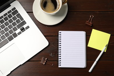 Photo of Notebook, sticky note, pen, binder clips, coffee and laptop on wooden table, flat lay