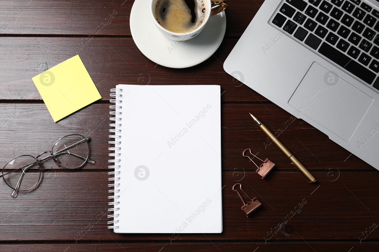 Photo of Notebook, sticky note, pen, binder clips, coffee, glasses and laptop on wooden table, flat lay