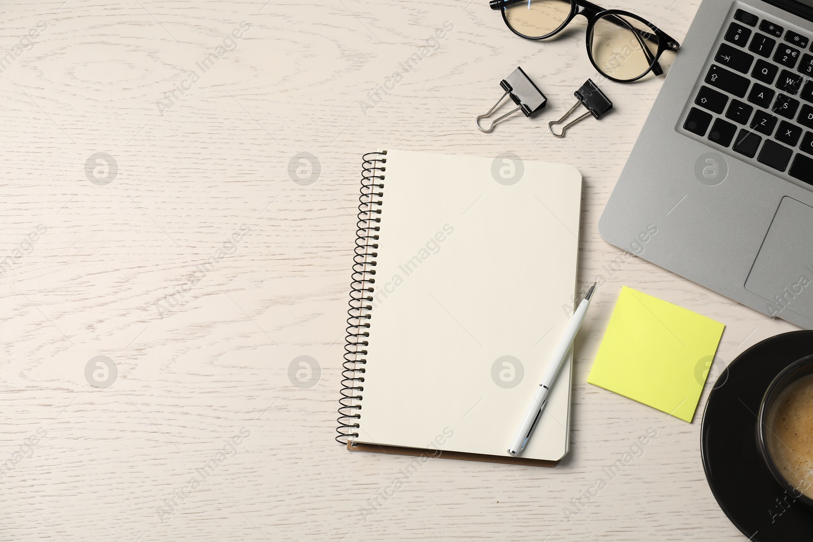 Notebook, pen, sticky note, binder clips, glasses, coffee and laptop on white wooden table, flat lay. Space for text Photo of Notebook, pen, sticky note, binder clips, glasses, coffee and laptop on white wooden table, flat lay. Space for text
