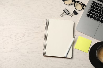 Photo of Notebook, pen, sticky note, binder clips, glasses, coffee and laptop on white wooden table, flat lay. Space for text
