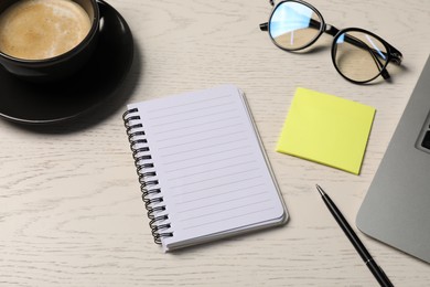 Photo of Notebook, pen, sticky note, glasses, coffee and laptop on white wooden table, above view