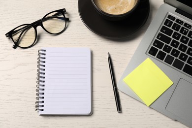 Photo of Notebook, pen, sticky note, glasses, coffee and laptop on white wooden table, flat lay