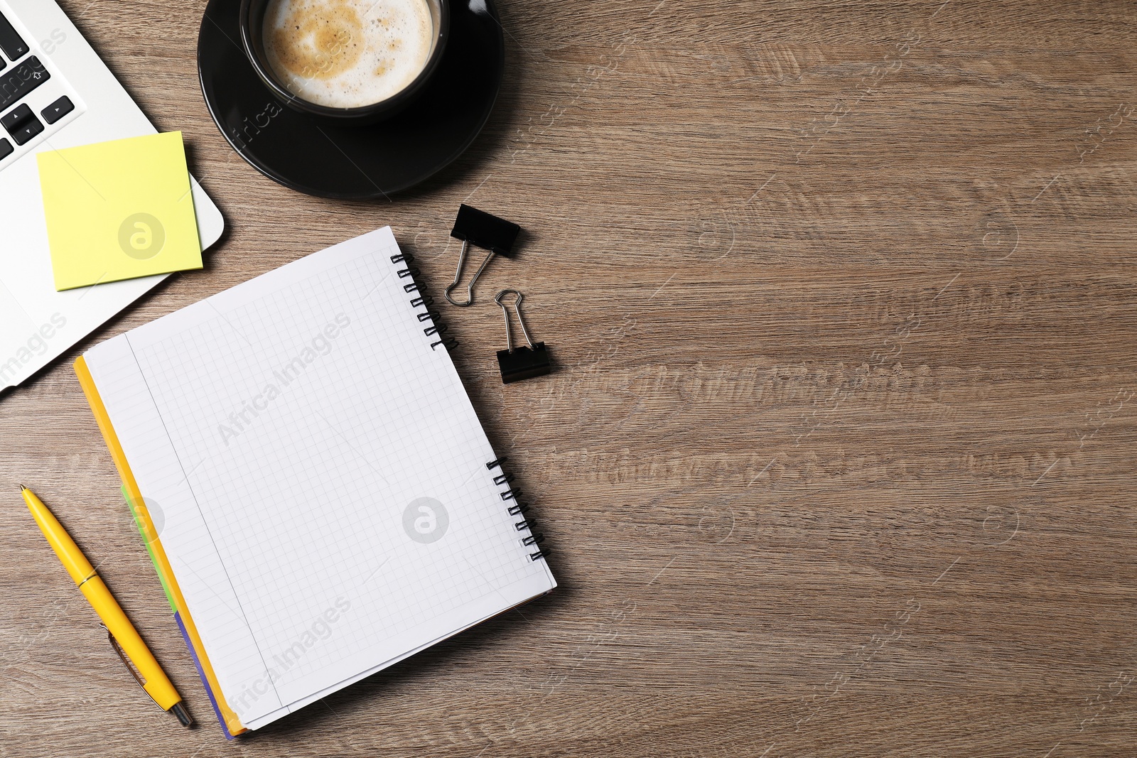 Photo of Notebook, sticky note, pen, binder clips, coffee and laptop on wooden table, flat lay. Space for text