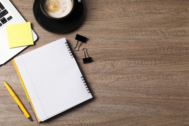 Photo of Notebook, sticky note, pen, binder clips, coffee and laptop on wooden table, flat lay. Space for text