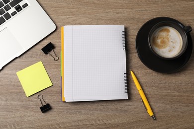 Photo of Notebook, sticky note, pen, binder clips, coffee and laptop on wooden table, flat lay