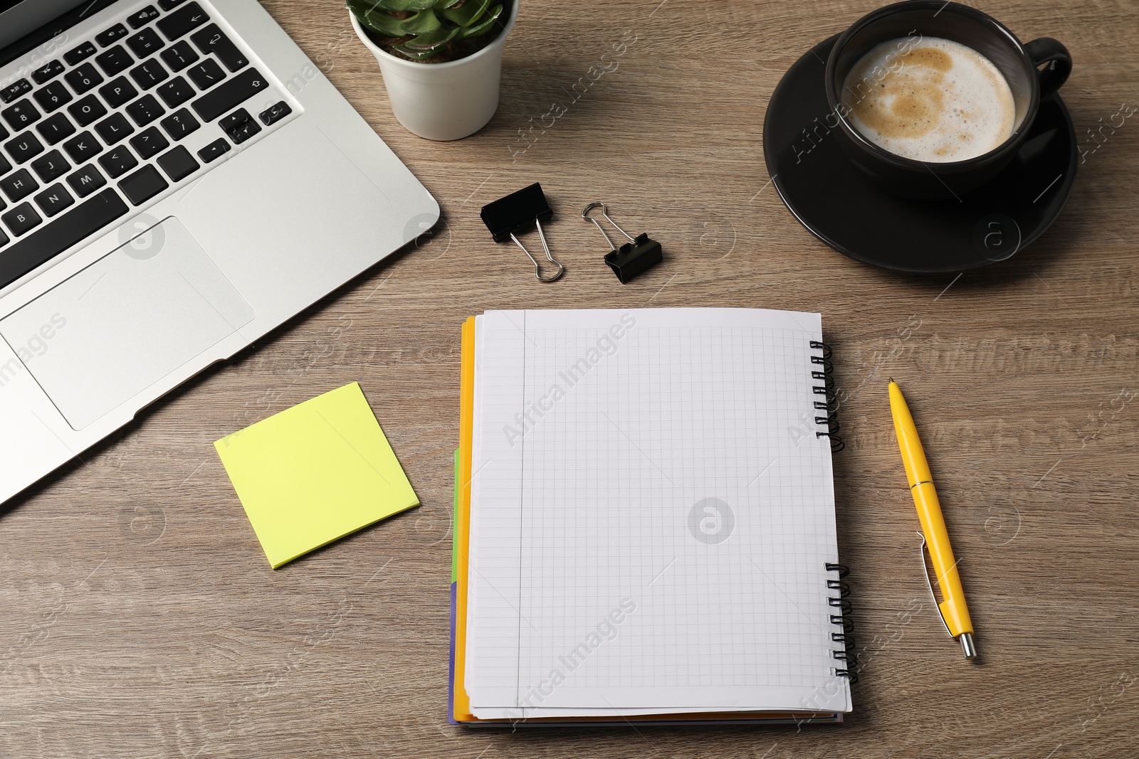 Notebook, pen, sticky note, binder clips, coffee, floral decor and laptop on wooden table, above view Photo of Notebook, pen, sticky note, binder clips, coffee, floral decor and laptop on wooden table, above view