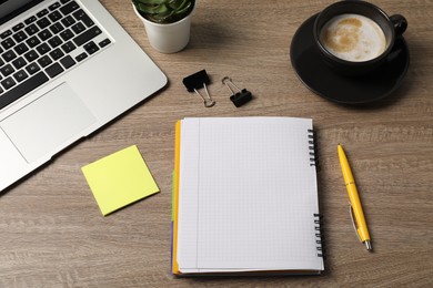 Photo of Notebook, pen, sticky note, binder clips, coffee, floral decor and laptop on wooden table, above view